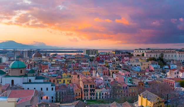 カリアリの夕日、伝統的な色の家、山々、空に美しい黄ピンクの雲、サルデーニャ島、イタリアの旧市街中心部のパノラマ