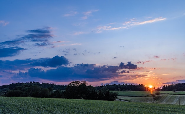 Sunset in a cloudy sky over a hilly rural valley with forests and wheat fields