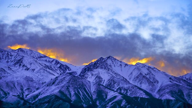 sunset in front of snowy mountains with sun in the clouds
