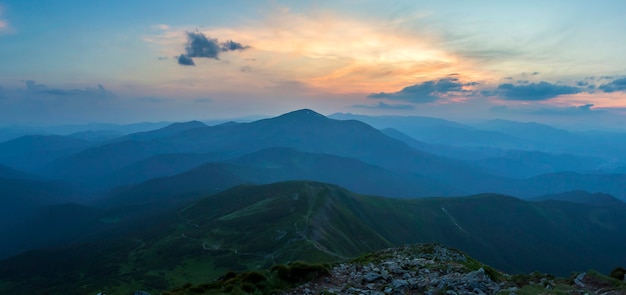 Sunset over green mountain ridge covered with dense blue fog