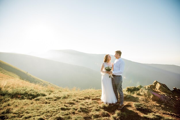 Sunset illuminates mountain hill where wedding couple walks