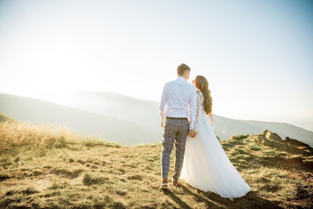 Sunset illuminates mountain hill where wedding couple walks