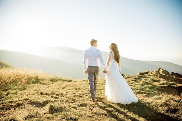 Sunset illuminates mountain hill where wedding couple walks