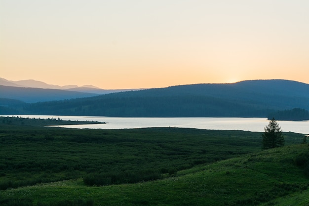 写真 山の湖の谷の夕日。葦に覆われた山脈と突き抜けない森に囲まれた美しい山の湖。