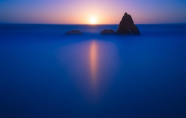 Foto un tramonto si riflette nell'acqua con una roccia in primo piano