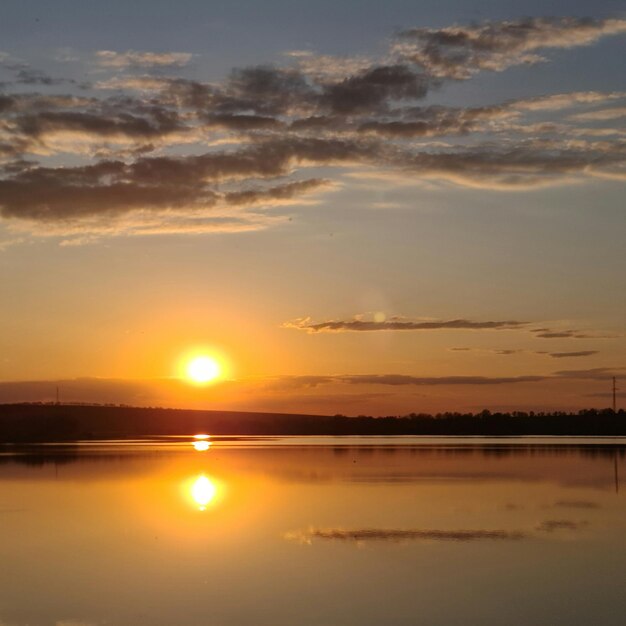 雲と数本の木々がある湖に沈む夕日。