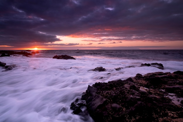 海の海と波を背景にしたビーチの夕日の風景-太陽と雲の劇的な空-夕暮れの光と地平線