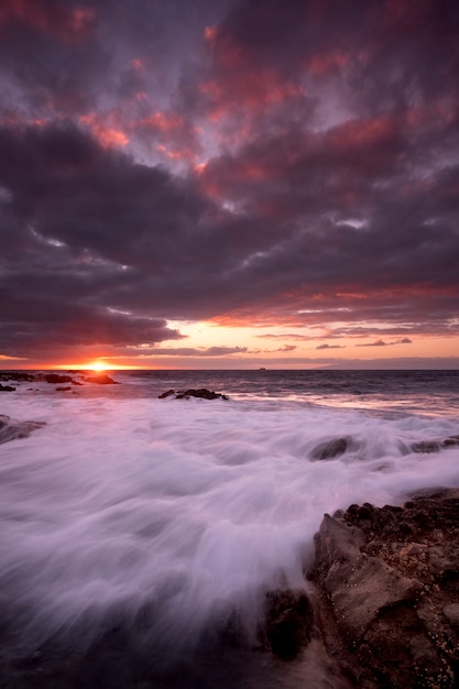 海の海と波を背景にしたビーチの夕日の風景-太陽と雲の劇的な空-夕暮れの光と地平線