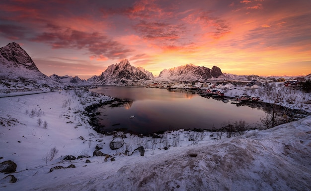 Sunset at Lofoten Islands in Norway with mountains covered in snow and reflection on the sea.