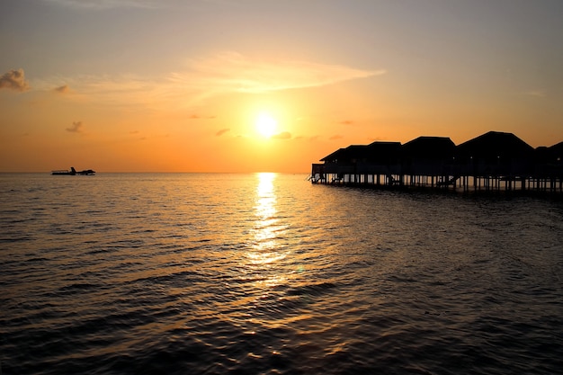 Sunset on Maldives island with water villa resort and reflection of sunlight on sea