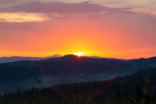 カルパティア山脈の山々に沈む夕日。太陽は山脈の後ろに沈みます。夕方の空に美しい色とりどりの雲。