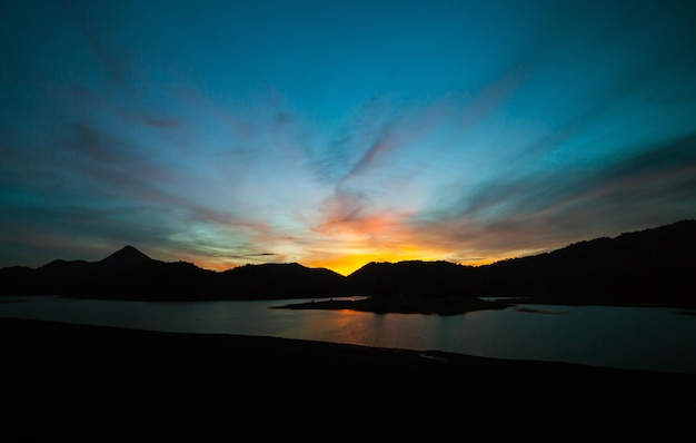 夕暮れ時に川と山の後ろに沈む夕日