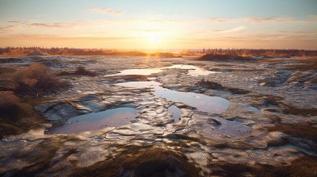 A sunset over a muddy field with a few puddles of water and the sun setting behind it.