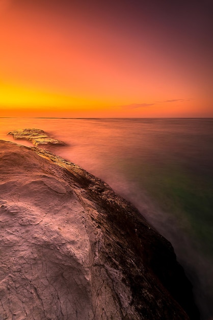 A sunset over the ocean with a rock in the foreground