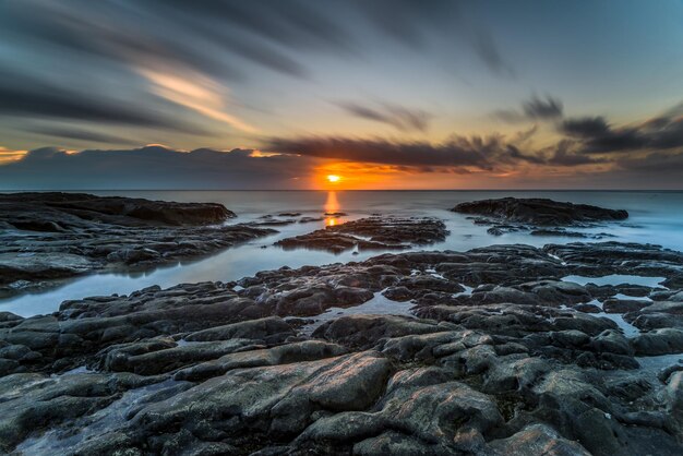 A sunset over the ocean with rocks and rocks in the foreground.