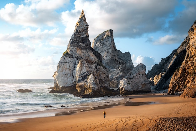 写真 ポルトガルの海岸の岩の間を散歩している男とシントラのウルサのビーチに沈む夕日