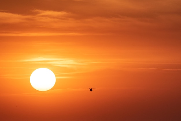 Sunset orange sky background at evening with clouds and silhouette of the helicopter