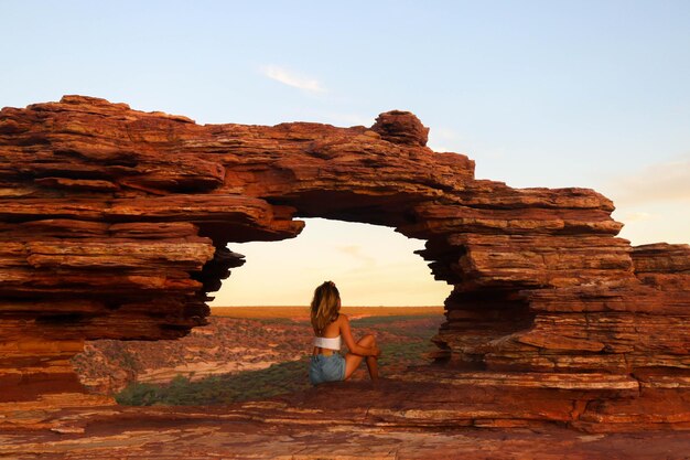 Sunset portrait of woman in natural red rock window with spectacular view