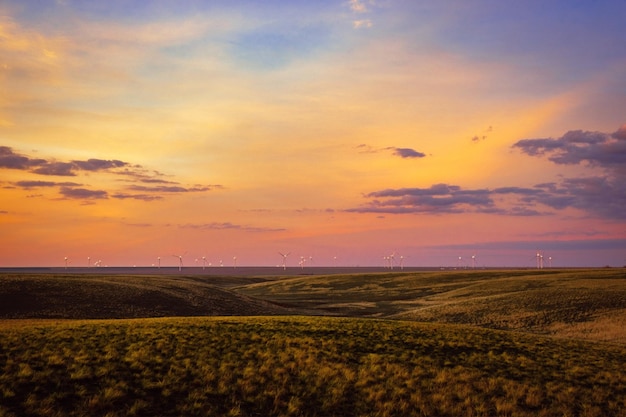 Foto un tramonto su una prateria con turbine eoliche in lontananza.