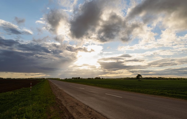 Sunset over the road between fields and meadows. Beautiful clouds. Horizontal photo.