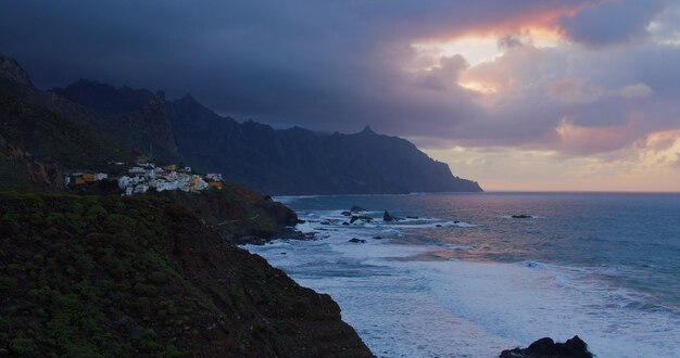 Photo sunset over rocks in the sea atlantic ocean waves with foam and giant volcanic formations in the background north of tenerife canary islands roques de anaga nobody