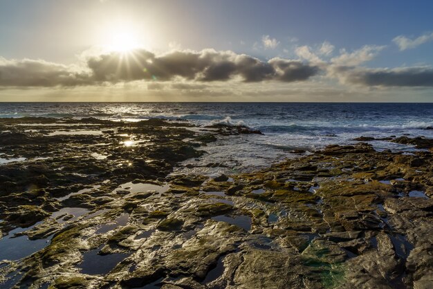 Sunset on the sea coast with large rocks washed by the waves, sky with clouds in golden tones and reflections in the water between the rocks. Spain. Europe.