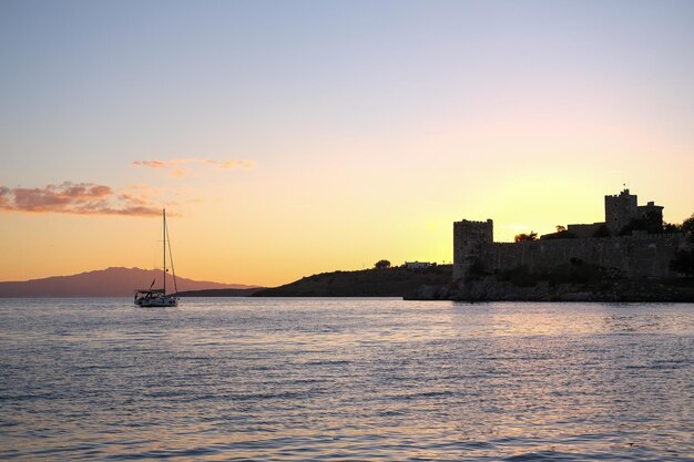 海に沈む夕日、要塞を背景にした地平線上のボートのシルエット、日の出