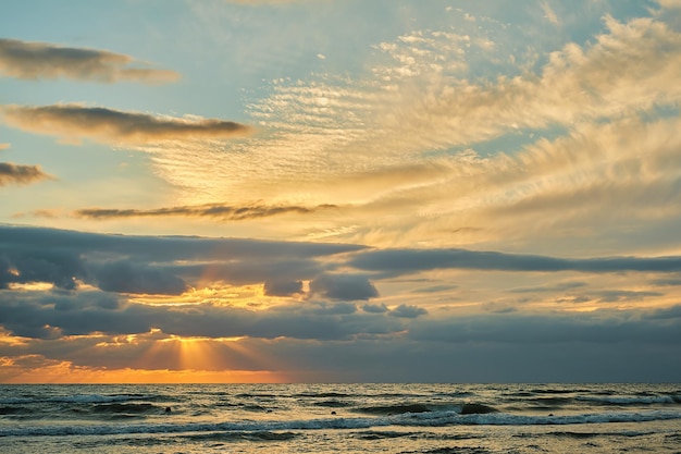 オレンジ色の日光の色とりどりの雲と夜遅くの海の上の夕焼け空太陽の光が雲の切れ間から輝く