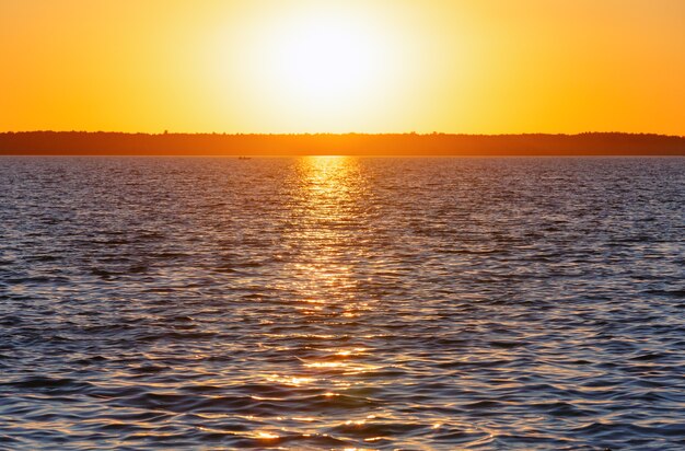 Sunset and sun track on summer lake surface.