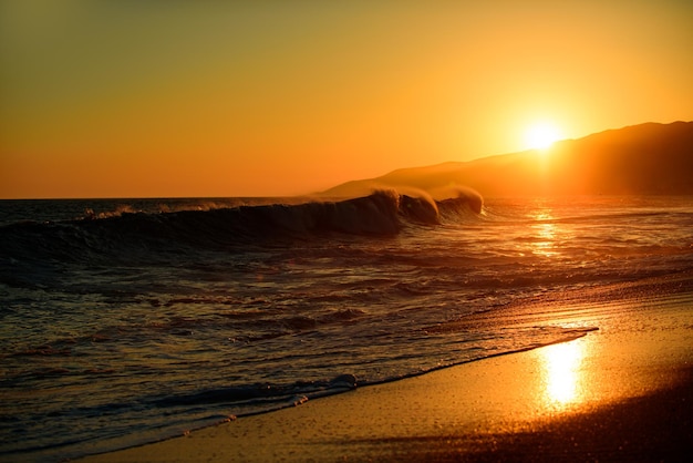 波の海のビーチに沈む夕日。日の出の夏の風景。