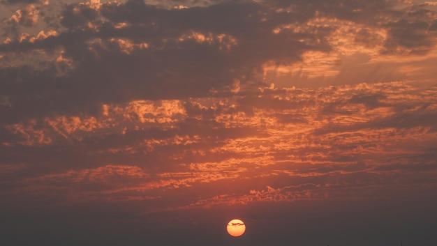 A sunset with a boat in the foreground and a purple sky with clouds in the background.