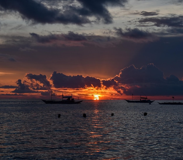 Photo a sunset with boats in the water and a sky with clouds