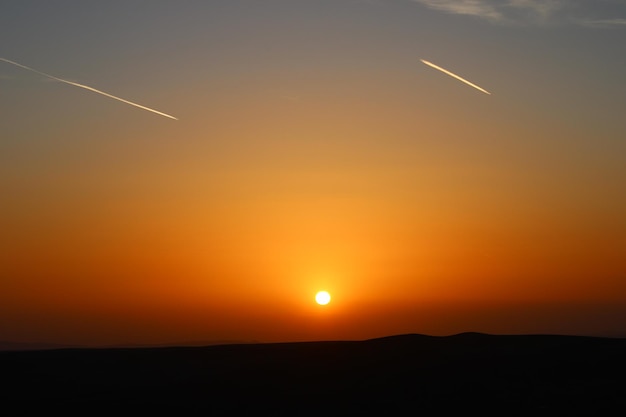 Photo a sunset with a plane flying in the sky and the plane trails in the sky