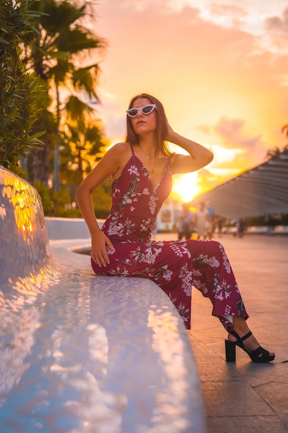 Sunset with a young brunette in a maroon floral dress and modern white sunglasses