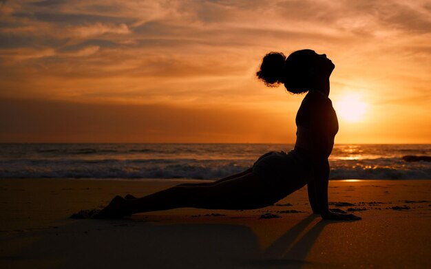 Sunset yoga fitness and silhouette of a woman at the beach for mindfulness training at night Meditation zen and girl stretching for a pilates pose at the sea in the evening for spiritual exercise