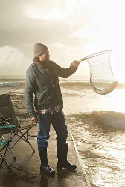 Sunshine net and beach with man fish and hobby with equipment waves and weekend break Person ocean and guy with tools for activity and happiness with shore pier and seaside with lens flare