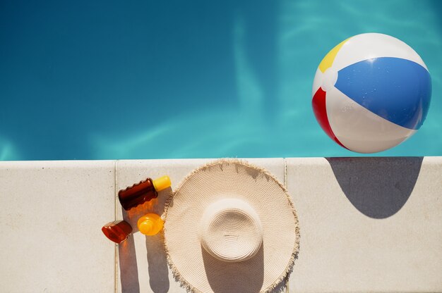 Suntan oil, hat and ball at the edge of the pool