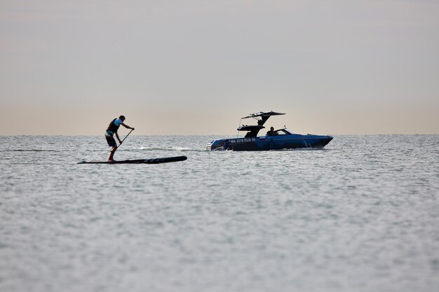 Sup surfer roeit op zee achter de motorboot aan.