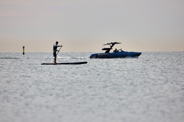 Sup surfer rows on the sea after the motor boat.