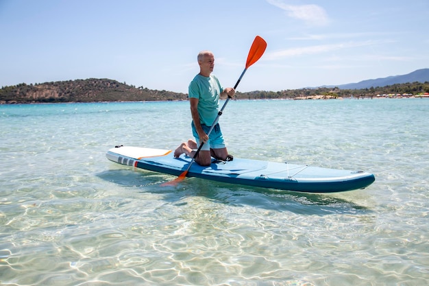 Foto super surfingbella vista del mare con un uomo maturo in ginocchio su una tavola con la pagaia in acqua