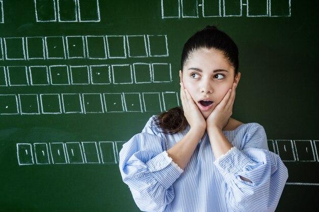 Photo supdrised girl in glasses stays near blackboard in classroom