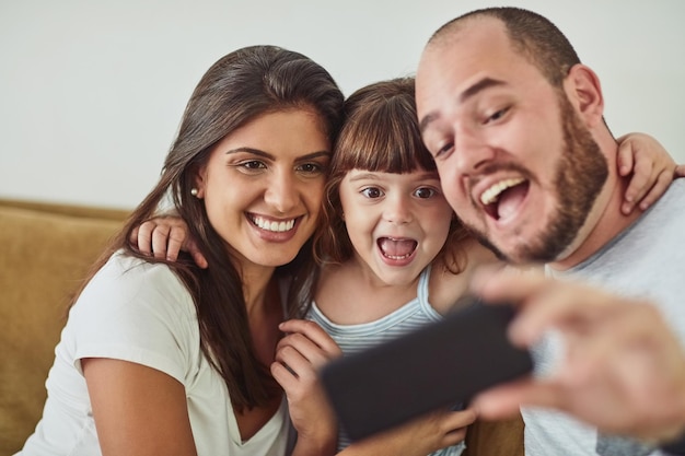 Super happy to spend time with the fam Shot of a mother and father taking selfies together with their young daughter at home