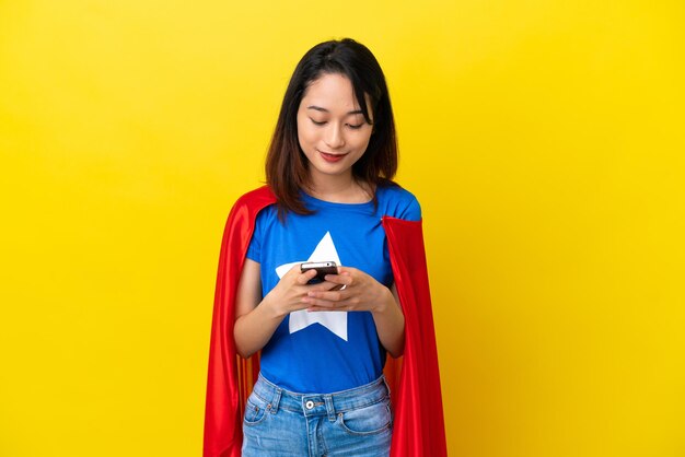 Super held Vietnamese vrouw geïsoleerd op gele achtergrond die een bericht verzendt met de mobiel