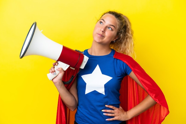 Super held vrouw geïsoleerd op gele achtergrond met een megafoon en denken