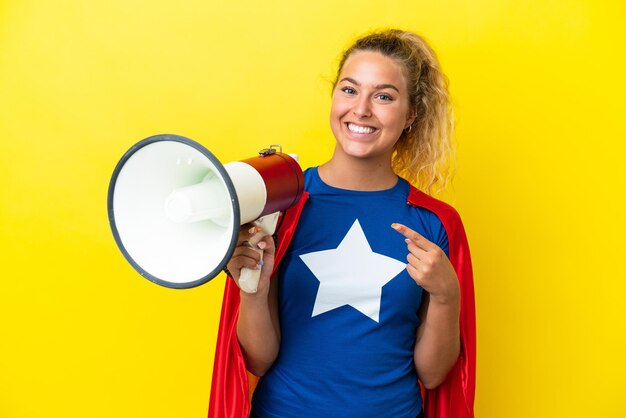 Super held vrouw geïsoleerd op gele achtergrond met een megafoon en wijzende kant