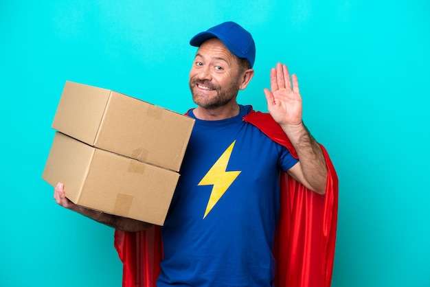 Super hero bezorger geïsoleerd op blauwe achtergrond die met de hand groet met een gelukkige uitdrukking