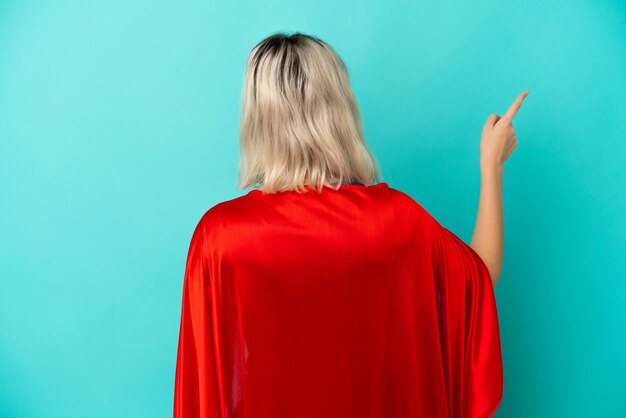 Super Hero blanke vrouw geïsoleerd op blauwe achtergrond die terug wijst met de wijsvinger