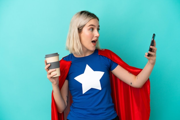 Super Hero blanke vrouw geïsoleerd op blauwe achtergrond met koffie om mee te nemen en een mobiel