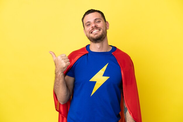 Super Hero Braziliaanse man geïsoleerd op gele achtergrond wijzend naar de zijkant om een product te presenteren present