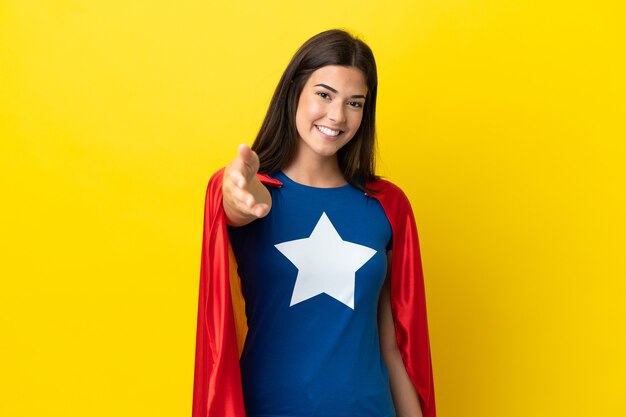 Super hero braziliaanse vrouw geïsoleerd op gele achtergrond handen schudden voor het sluiten van een goede deal